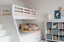 a lovely shared girls’ bedroom with a pink wallpaper ceiling, a white bunk bed with bold bedding, a storage unit and some art