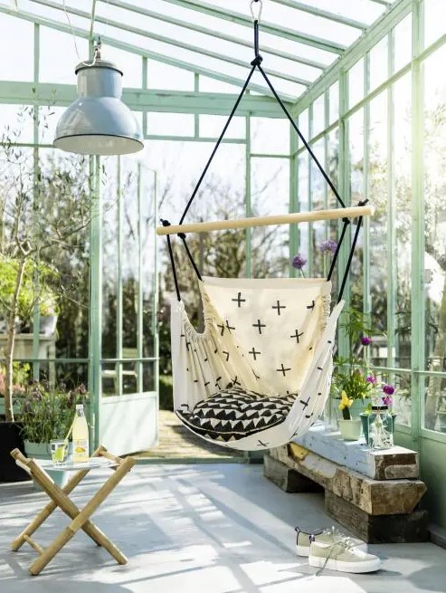 a lovely sunroom or glass house with a pendant chair, some stools, a reclaimed wooden bench with potted blooms is cool