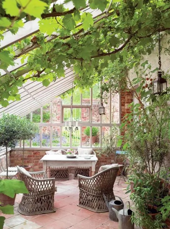 a lovely vintage sunroom with a tiled floor and brick walls, vintage furniture including rattan chairs and potted greenery everywhere