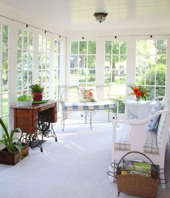 a lovely vintage sunroom with wooden and forged furniture, printed upholstery, potted greenery and blooms
