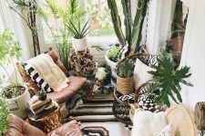 a lush boho sunroom with leather chairs, lots of potted greenery and some wicker and woven touches