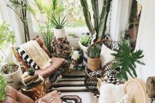 a lush boho sunroom with leather chairs, lots of potted greenery and some wicker and woven touches