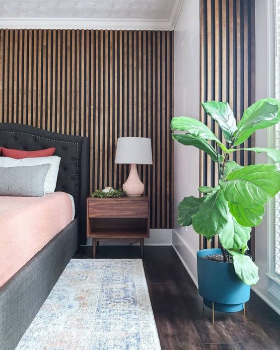 a mid century modern bedroom with a wood slat accent wall, a graphite grey upholstered bed and a stained nightstand