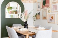 a mid-century modern dining room with a green accent and a mirror, a bright gallery wall, a blonde wood table and grey chairs