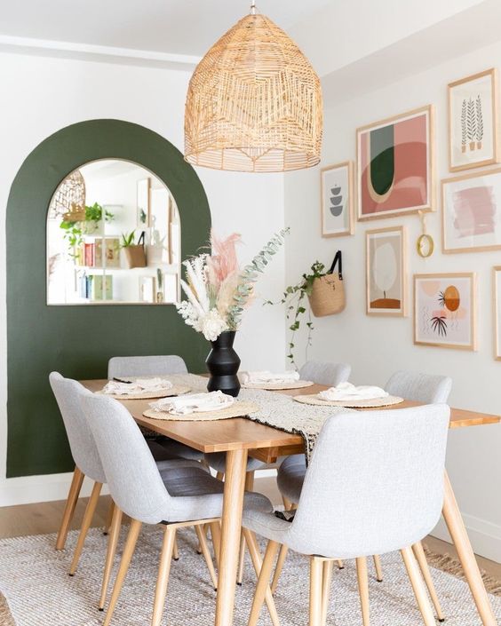 a mid-century modern dining room with a green accent and a mirror, a bright gallery wall, a blonde wood table and grey chairs