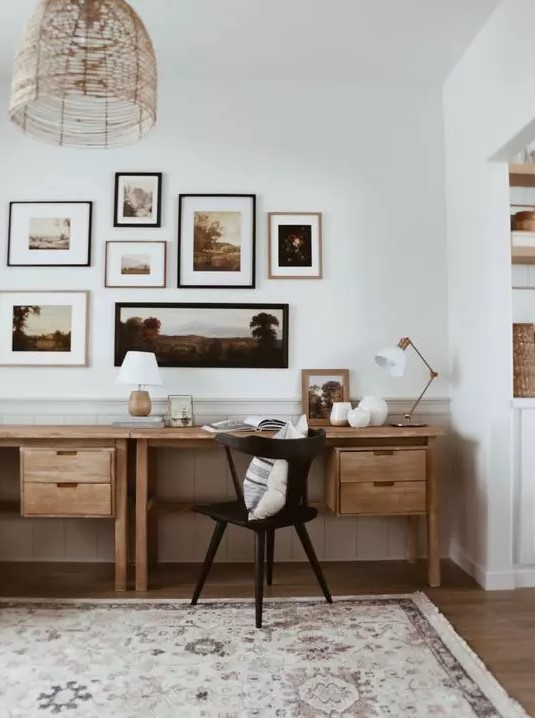 a mid century modern home office with a shared stained desk, a black chair, a moody gallery wall and a woven pendant lamp