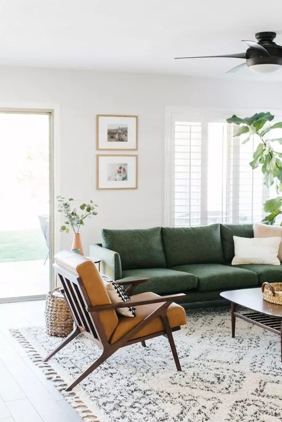 a mid century modern living room with a green sofa, a brown leather chair, a mini gallery wall and some greenery