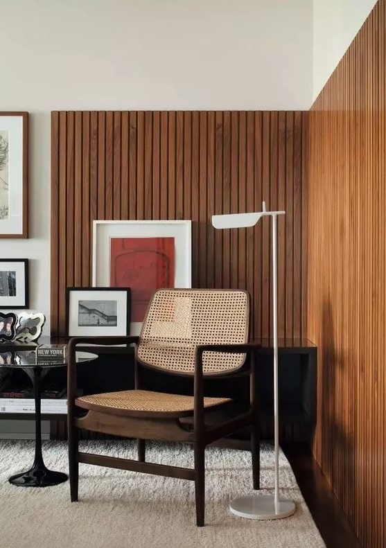 a mid century modern living room with stained wood slat accent walls, a rattan chair, a black table and bright artwork