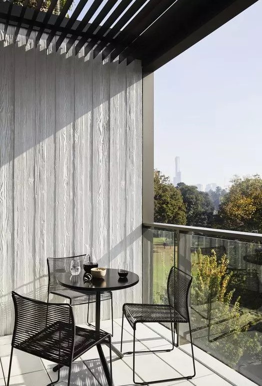 a minimalist balcony with a black round table and black metal chairs, with a lovely garden view is a cool space to have a meal