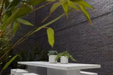 a minimalist outdoor dining space with a large concrete table and benches and potted greenery is a sleek and edgy nook