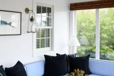 a modern beachy sunroom with a blue L-shaped sofa, black pillows, wooden tables and candles and art