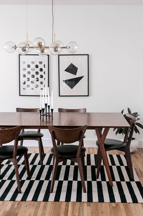 a modern dining space with a stained table and chairs, a black and white rug, a mini gallery wall and a mid-century modern chandelier