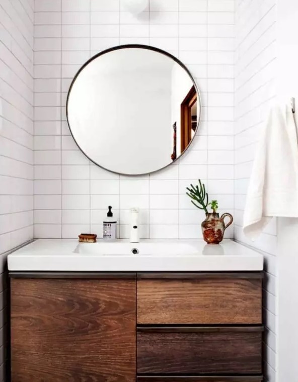 a modern farmhouse bathroom with stacked white tiles, a dark-stained built-in vanity and a round mirror is all cool