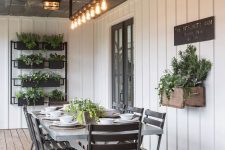 a modern farmhouse sunroom with planked walls, a trestle dining table and black chairs, potted greenery on the wall