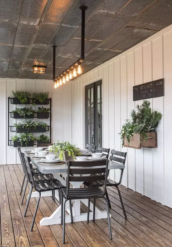 a modern farmhouse sunroom with planked walls, a trestle dining table and black chairs, potted greenery on the wall