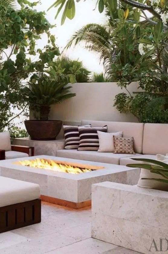 a modern outdoor living room with a neutral sofa and matching chairs, a concrete chair and a fire pit