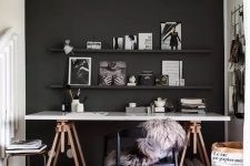 a moody home office with a black accent wall, a trestle deck, a black chair and a stool, a ledge gallery wall and a grid memo board