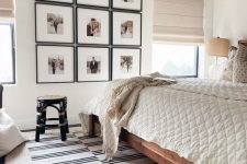 a neutral bedroom with a boho feel, a stained bed with neutral bedding, a grid gallery wall and layered rugs, a black rattan stool