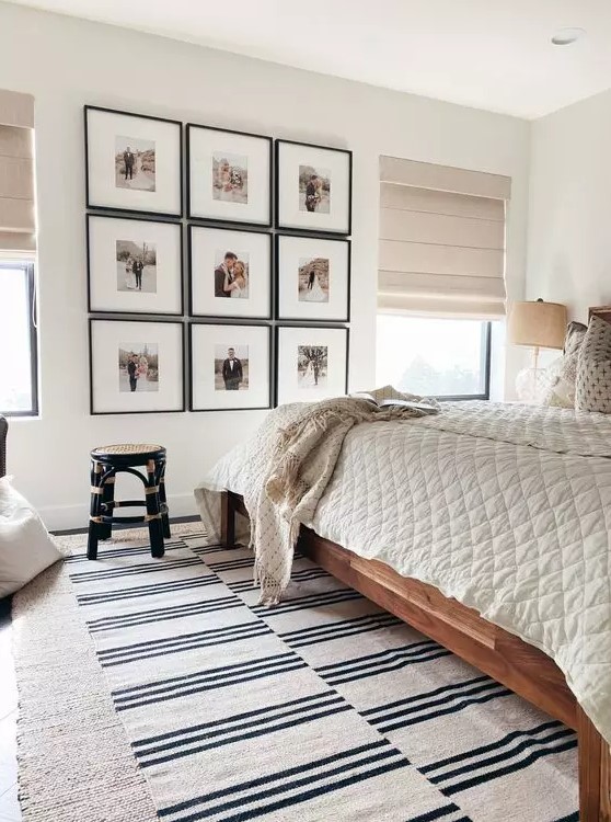 a neutral bedroom with a boho feel, a stained bed with neutral bedding, a grid gallery wall and layered rugs, a black rattan stool
