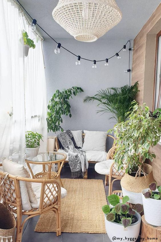 a neutral boho sunroom with grey walls, rattan furnitur,e potted plants, a glass coffee table and a woven pendant lamp