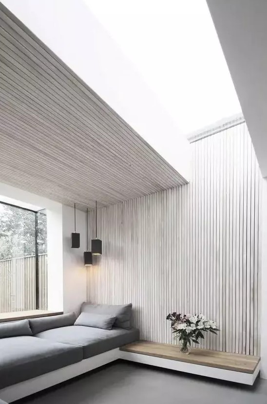 a neutral minimalist space with whitewashed wood slat walls and a ceiling, a grey upholstered daybed and black pendant lamps, a floating nightstand
