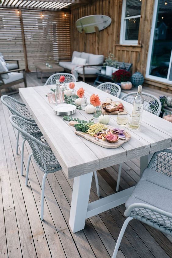 a neutral outdoor dining zone with a whitewashed table and white metal chairs with neutral cushions plus bold blooms on the table