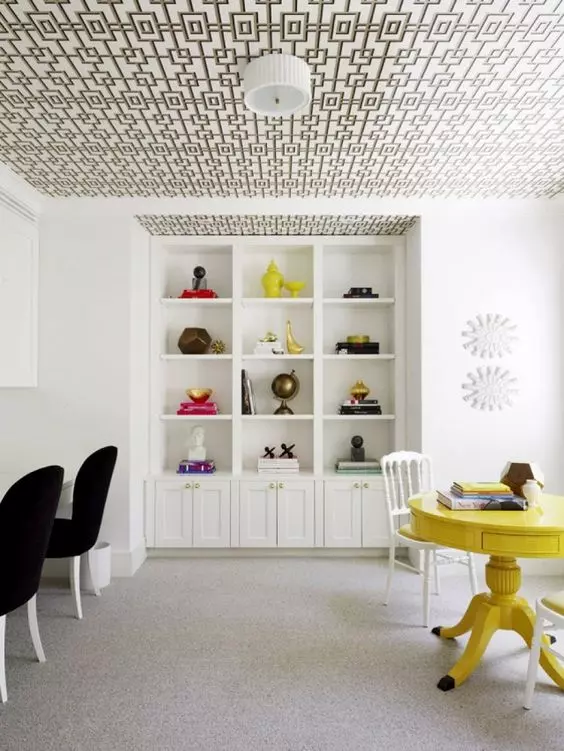 a neutral space with a wallpaper ceiling, built in storage units, black chairs, a yellow table and some lamps