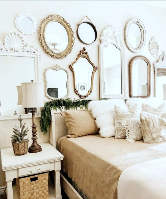 a neutral vintage bedroom with white vintage furniture, neutral and printed bedding, a gallery wall or mirrors of various shapes