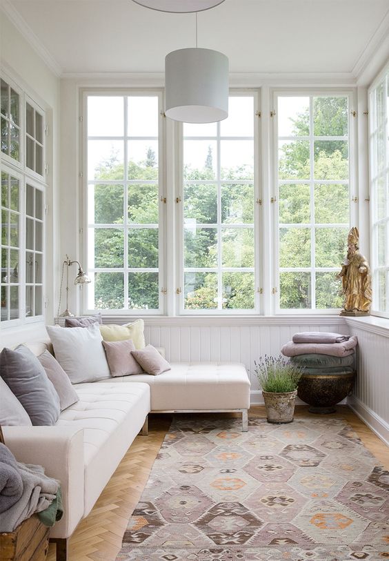 a peaceful Scandinavian sunroom with a neutral corner sofa with pillows, potted lavender, blankets and some decor