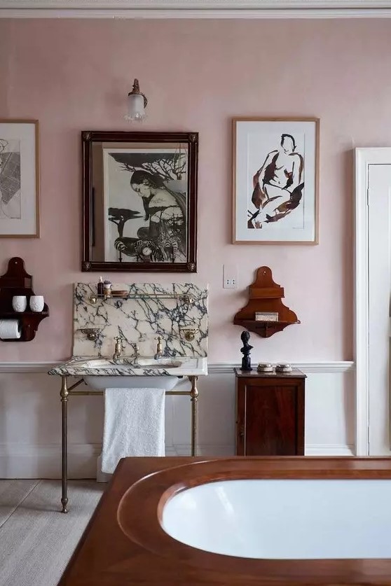a pink bathroom with limewashed walls, a tub, a free standing sink, wooden shelves and a gallery wall