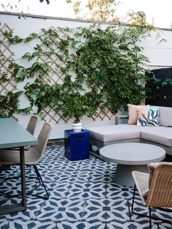 a pretty and bright terrace with tiles on the floor, a concrete table and wicker chairs, a corner sofa and a round table