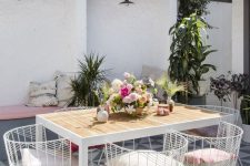 a pretty outdoor dining space with built-in benches, a white metal and wood dining table, white metal chairs and potted plants and blooms