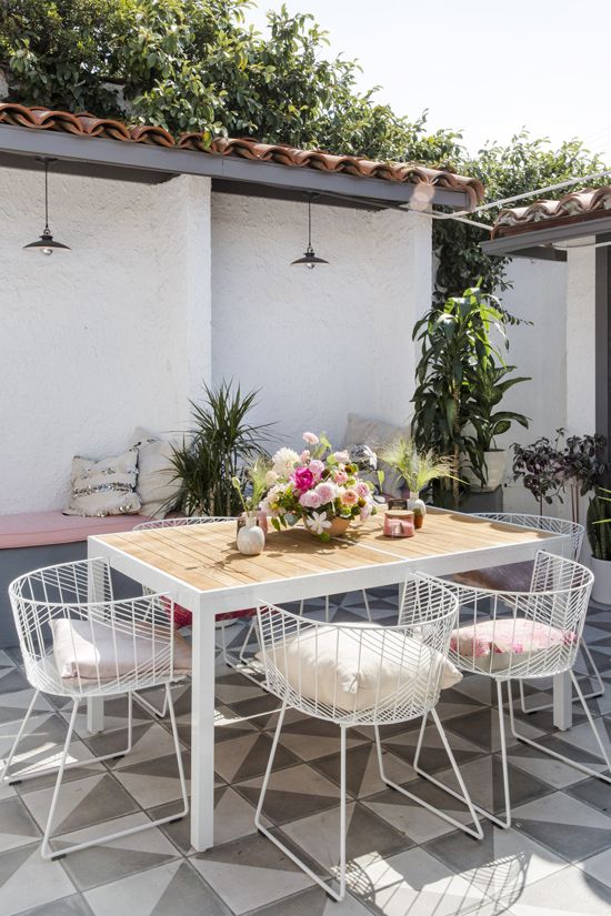 a pretty outdoor dining space with built-in benches, a white metal and wood dining table, white metal chairs and potted plants and blooms