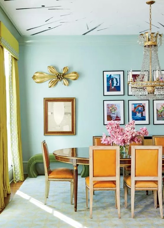 a quirky colorful dining room with mint green walls, a chic polished table and orange chairs, a statement chandelier and a grid colorful gallery wall