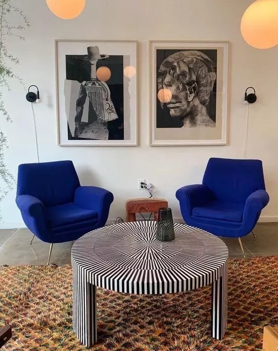 a quirky space with cobalt blue chairs, a striped round table, a colorful rug and a black and white gallery wall