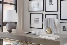 a refined home office with a grey stone desk, a grey and a creamy chair, a table lamp and a large gallery wall with matting and black frames