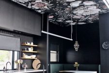 a refined moody kitchen with black walls and cabinets, a dark floral wallpaper ceiling, a black and white kitchen island