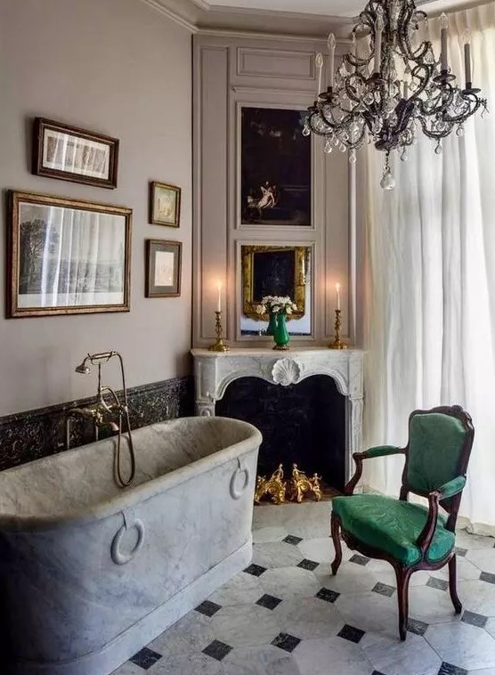 a refined vintage bathroom with a stone bathtub, a non working fireplace, a green chair, a refined crystal chandelier and a gallery wall