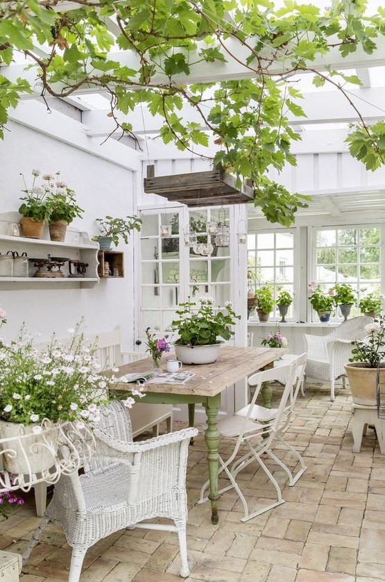 a refined vintage sunroom with white furniture   wicker and metal, a green table, potted greenery and blooms and hanging lamps