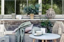 a relaxed outdoor space with a concrete daybed with pillows, a concrete side table and a coffee table, some lanterns and greenery