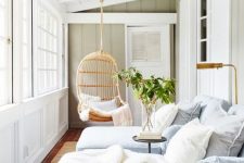 a relaxing small sunroom with striped blue lounge chairs, a lamp, a table and a hanging wicker chair