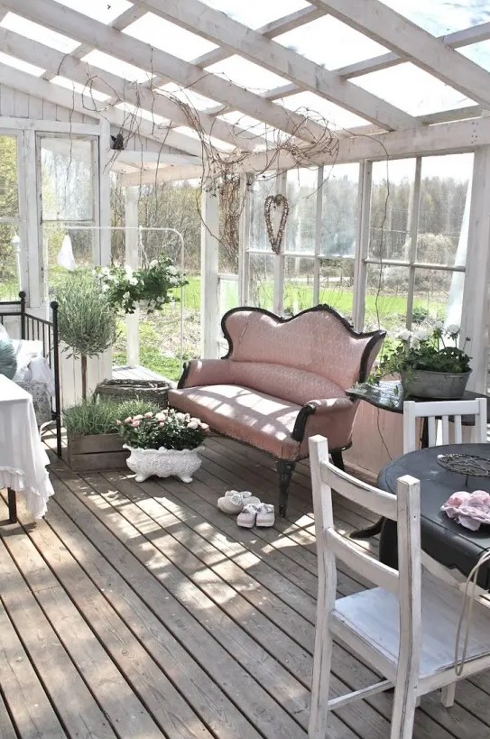 a sahbby chic attic sunroom with very refined vintage furniture, a dining, sleeping and relaxing zone, potted greenery and blooms