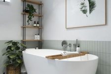 a serene neutral bathroom with a light green tile stacked backsplash, a terrazzo floor, an oval tub, potted plants and a bold artwork