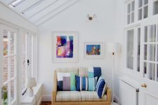 a simple and modern sunroom with a small wicker sofa with colorful pillows, artworks and a coffee table