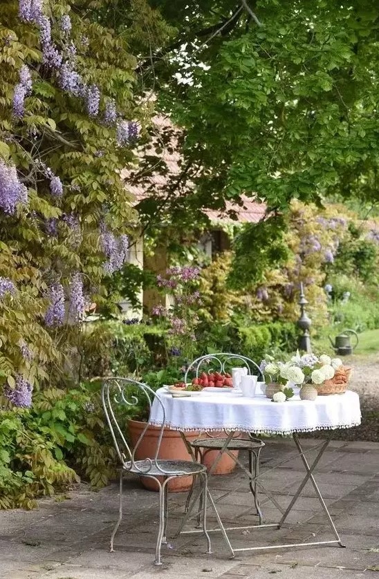 a small and lovely Provencal outdoor space with a metal table and chairs and some blooms and greenery around - who needs more than that