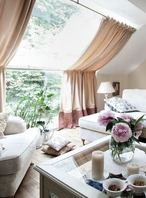 a small and lovely sunroom with a skylight and a large window, neutral seating furniture and a coffee table, potted blooms and plants