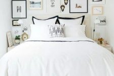 a small and stylish bedroom with a white bed and black and white bedding, a cool free form gallery wall and neutral nightstands and gold touches