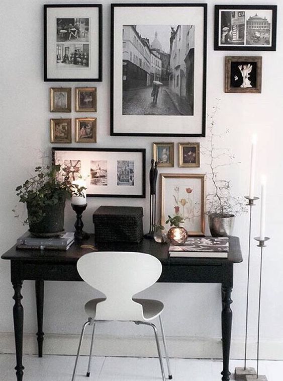 a small black and white working space with a refined black desk, a white chair, a black and white gallery wall and some plants