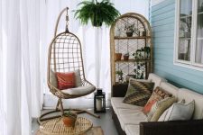 a small boho sunroom with a dark sofa, wicker furniture and a hanging chair plus potted greenery