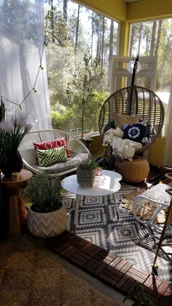 a small boho sunroom with a pendant chair, a woven chair, round coffee tables, pritned textiles and string lights plus potted plants